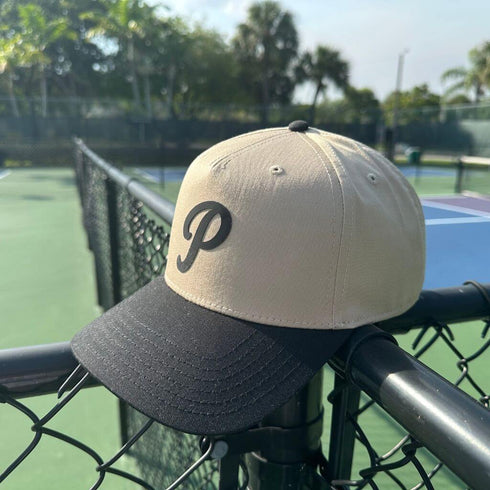 Beige and black cap with a 'P' logo on a tennis court fence